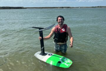 Rider holding a hydrofoil board while standing waist deep in the shallow Laguna Madre flats