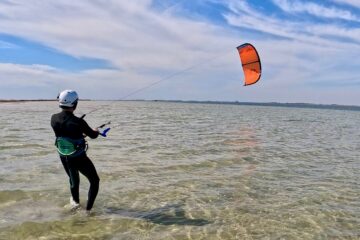 Kiteboarding student in a helmet flying an orange kite in shallow standing depth water near North Padre Island