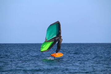 Wing foiler riding on a hydrofoil with a green inflatable wing